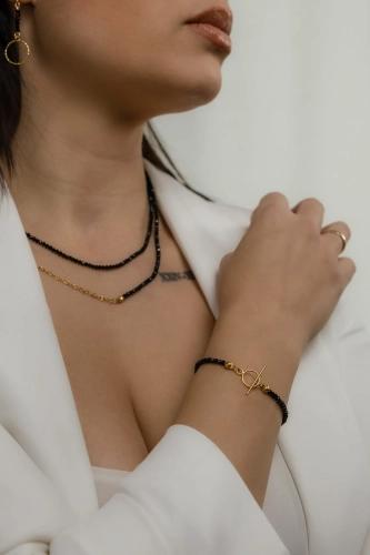 Bransoletka NINA BLACK z czarnych onyksów i złoconym zapięciem toggle na nadgarstku modelki